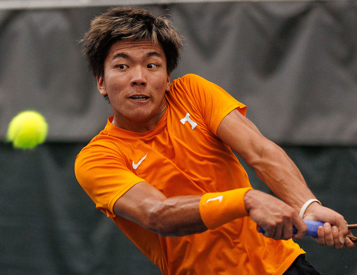 Tennessee Volunteer male tennis player, wearing orange and ranked in the men's college tennis rankings, hits a backhand during a UTR Sports college tennis event