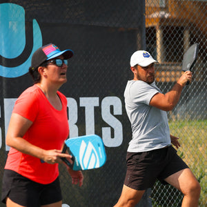 Two people playing pickleball on a court with a 'UTR Sports' banner in the background.