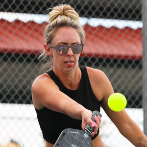 Woman playing pickleball on an outdoor court with a red roofed shelter in the background.